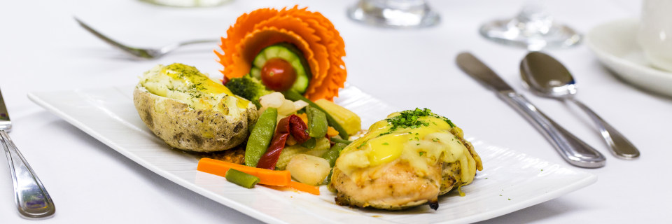 LUC banquet hall / wedding hall catering food, silverware and glasses. Garnished baked potato, sauteed vegetables, stuffed chicken breast covered with two kind of melted cheese and sprinkled with parsley or cilantro.