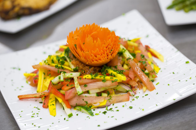 Decoratively composed plate of fruit and vegetable julienne salad sprinkled with cilantro, featuring a carrot floral decoration on top. LUC banquet hall / wedding hall catering sample food photo.